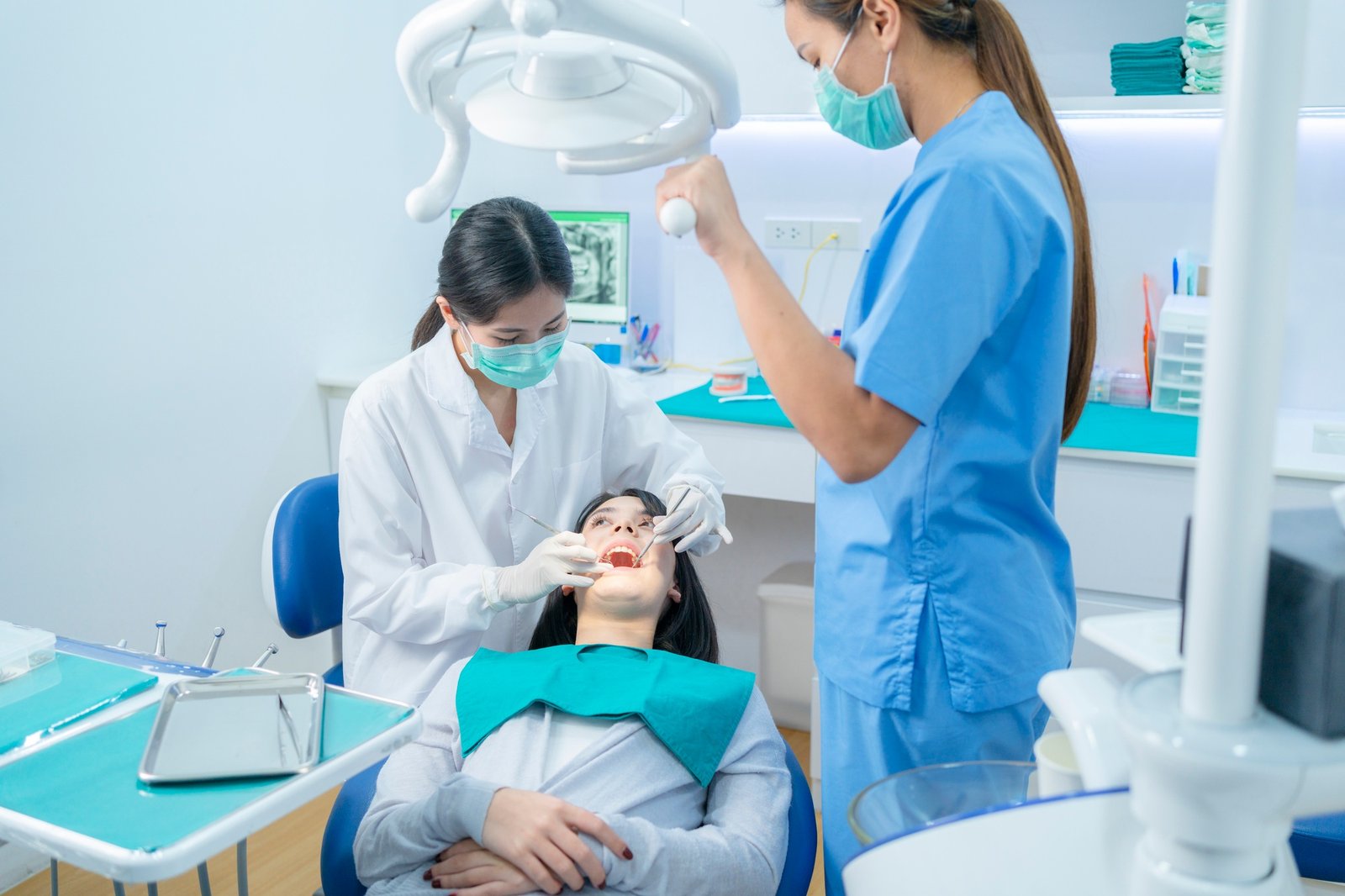 Asian dentist adjust dental surgical light then starts examining tooth patient at dental clinic