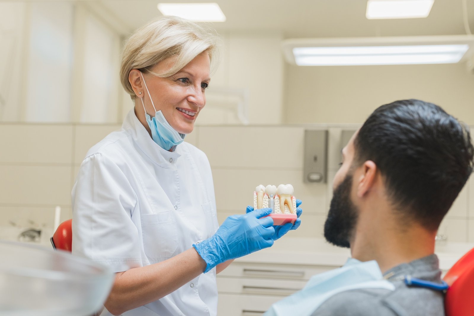 Dentist showing explaining to patient dental teeth tooth root implantation, caries cure in clinic