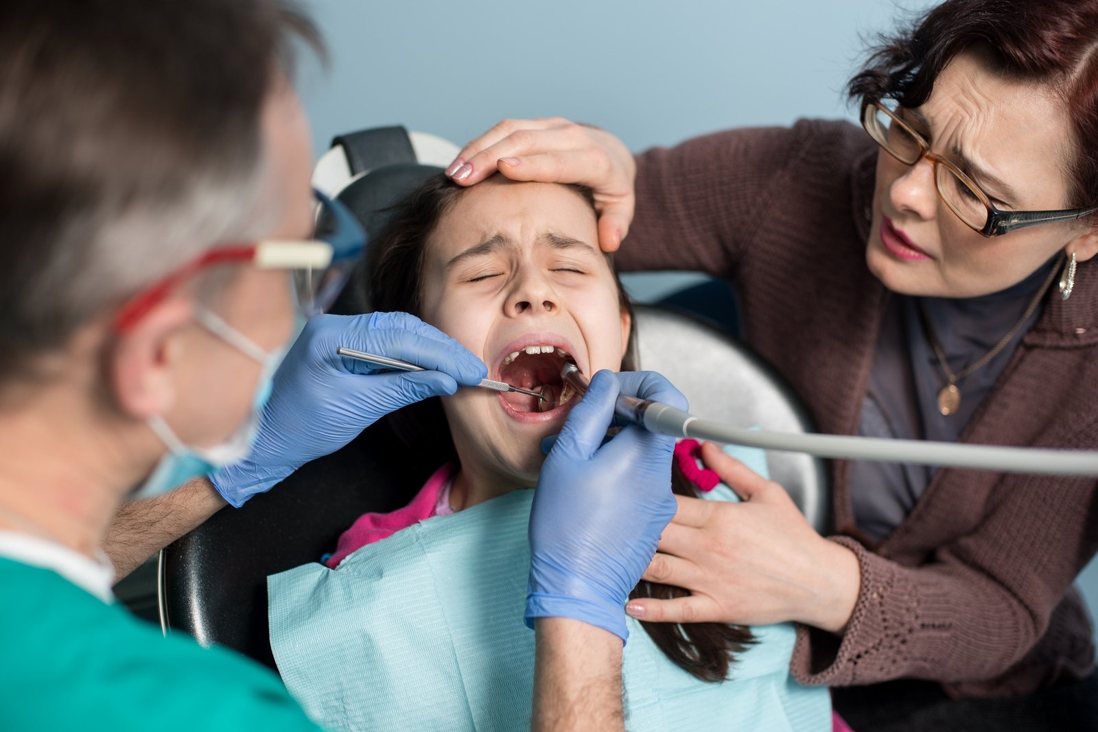 Girl with on the first dental visit. Senior pediatric dentist with mother treating patient teeth