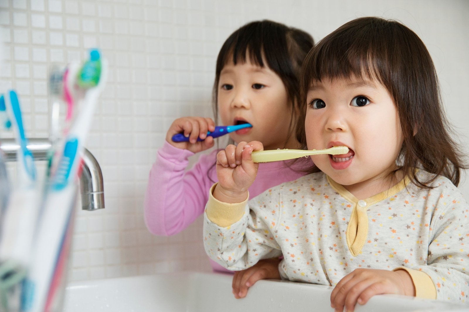 Two girl toddlers brushing teeth at bathroom sink